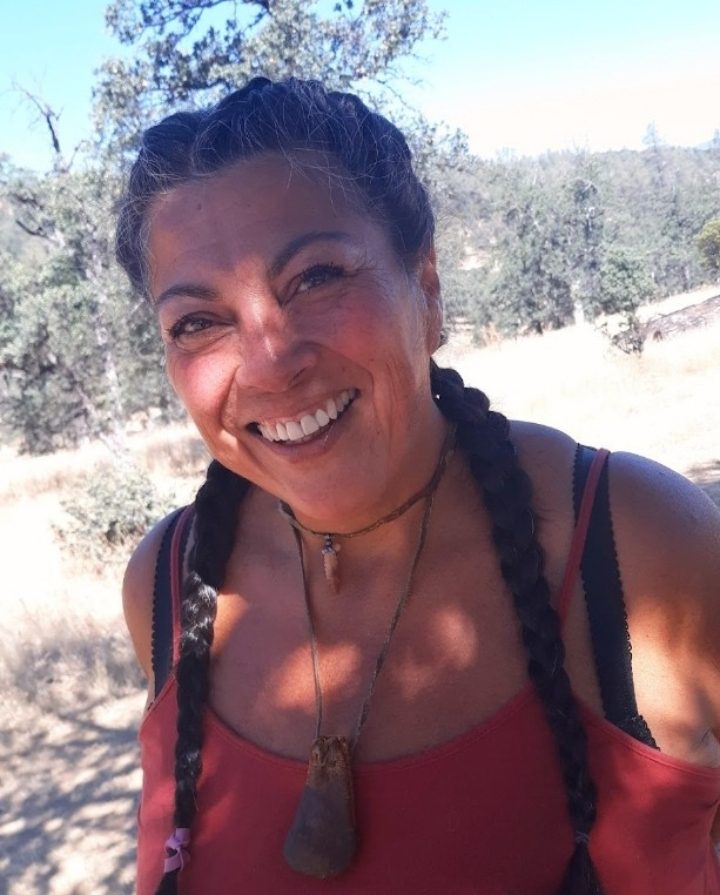 Denise Flores (Breese), smiling, hair in braids, in the oak woodland of R-Wild Horse Ranch